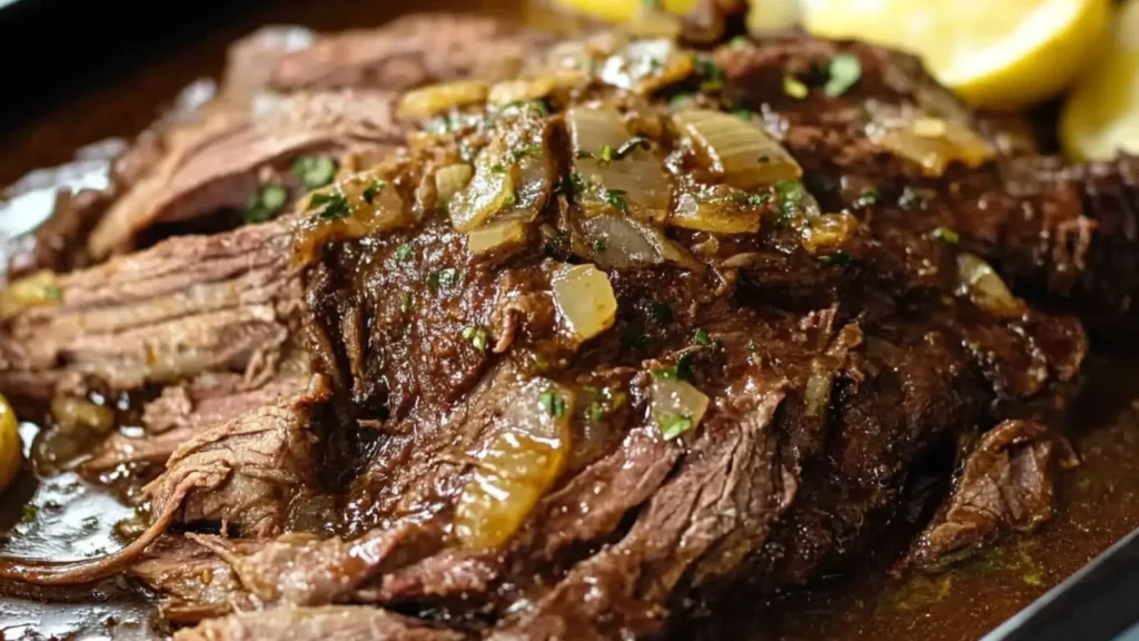 Close-up of a tender Mississippi roast topped with onions and gravy, served on a platter.
